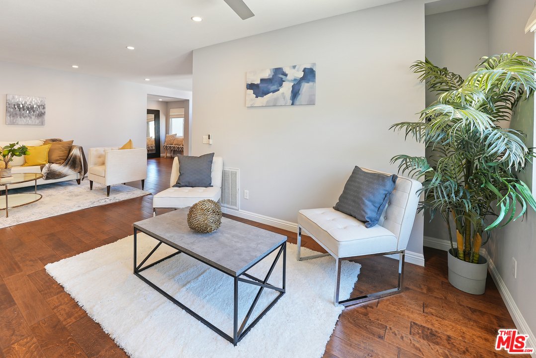Living room with wood floor, coffee table, white chairs, plant, and wall art.