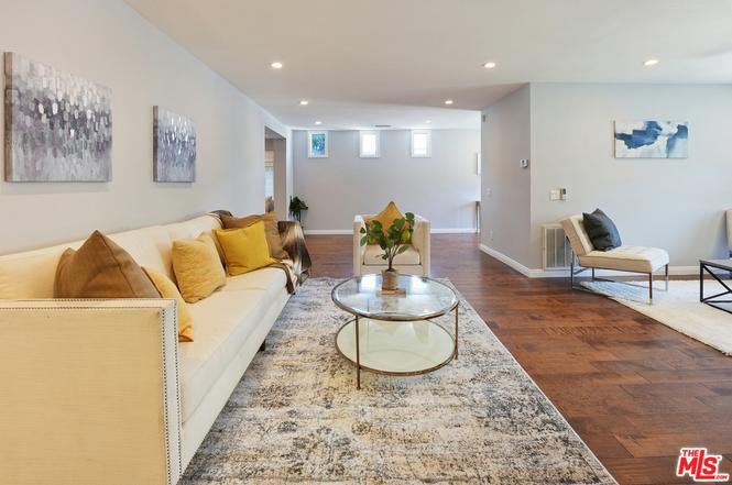 Living room with light sofa, pillows, glass coffee table, rug, wall art, and windows.