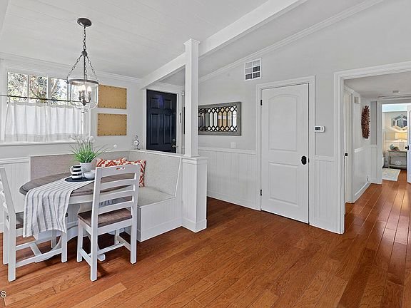 Dining area with round table, white chairs, striped tablecloth, wall decor, doorway, and wood floor.