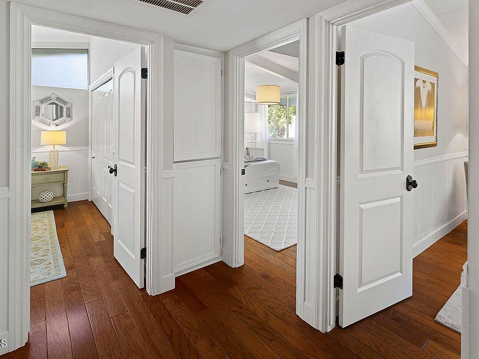 Hallway with white doors, wood floor, and soft ceiling lights.