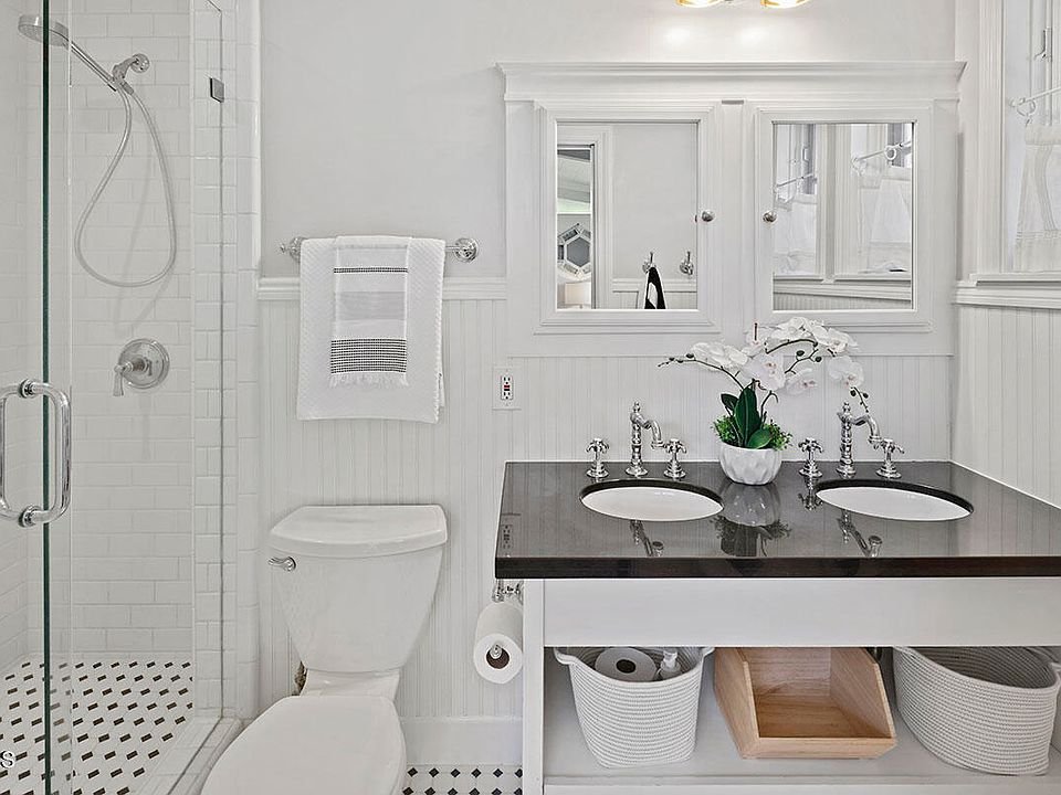 Bathroom with glass shower, white tiles, double sink vanity, large mirror, orchid plant, and towels.