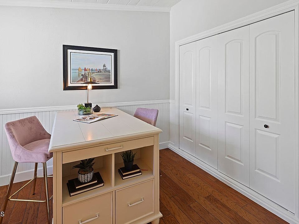Small room with white table, two pink chairs, wall picture, closet with double doors, and wood floor.