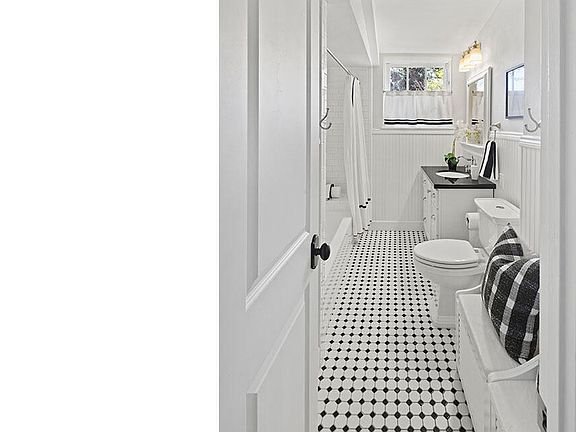 Bathroom with black and white tile floor, toilet, sink, shower, and window.