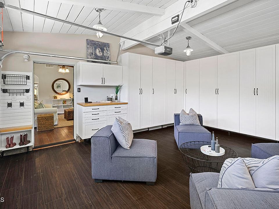 Room with two gray chairs, round table, white cabinets, doorway, and dark wood floor.