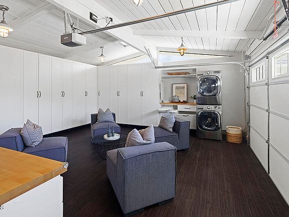 Laundry room with two washers, white cabinets, wood floor, gray chairs, and small round table.