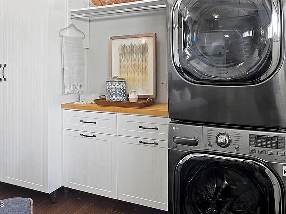 Laundry room with black washer and dryer, white cabinets, wood counter, and decor.