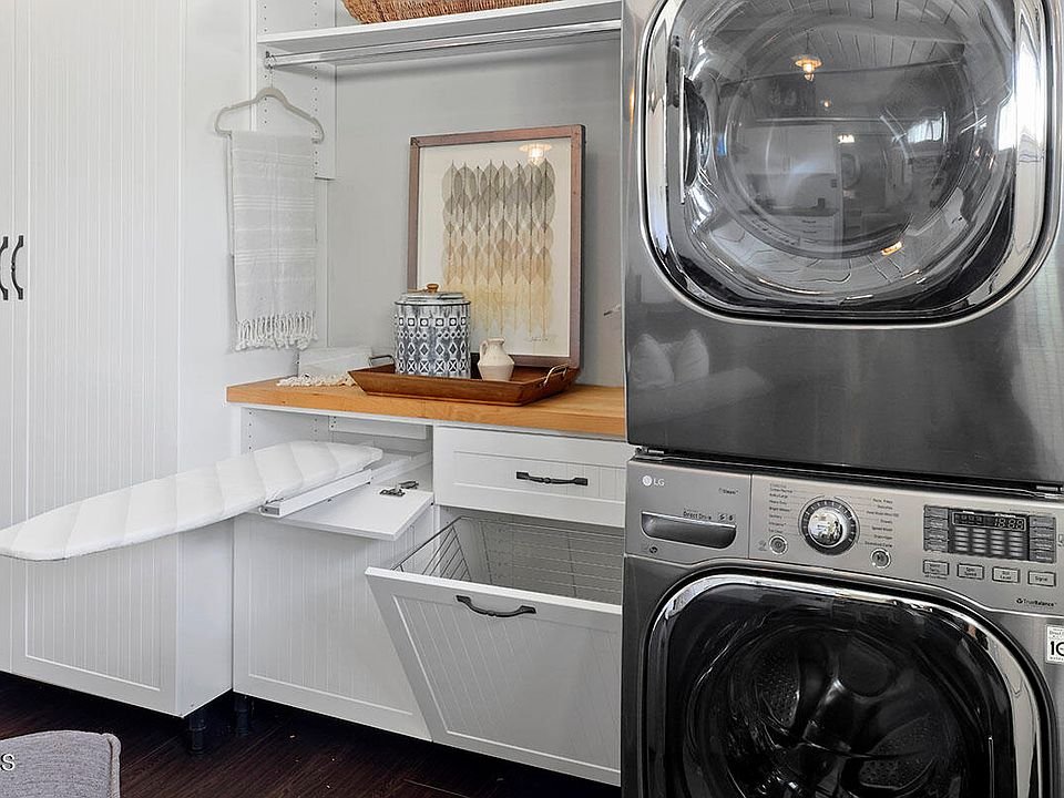 Laundry area with stacked washer and dryer, white cabinets, counter, and pull out ironing board.