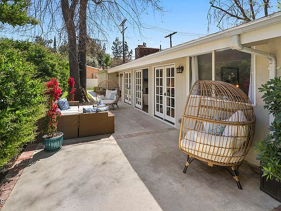Outdoor seating with wicker chairs, flowers, green plants, and big glass doors to house California real estate.