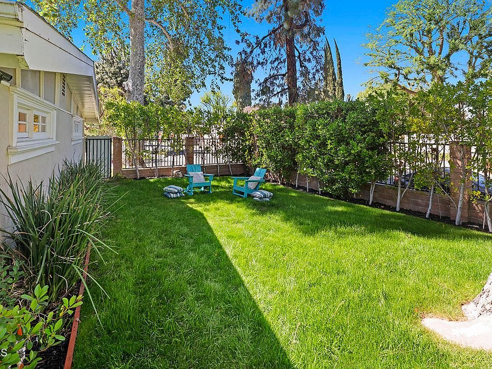 Yard with green grass, two blue chairs, and tall trees.