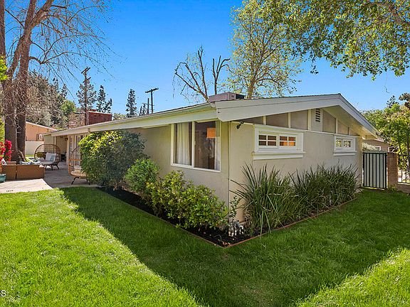 Single story house with flat roof, green lawn, and shrubs California real estate.