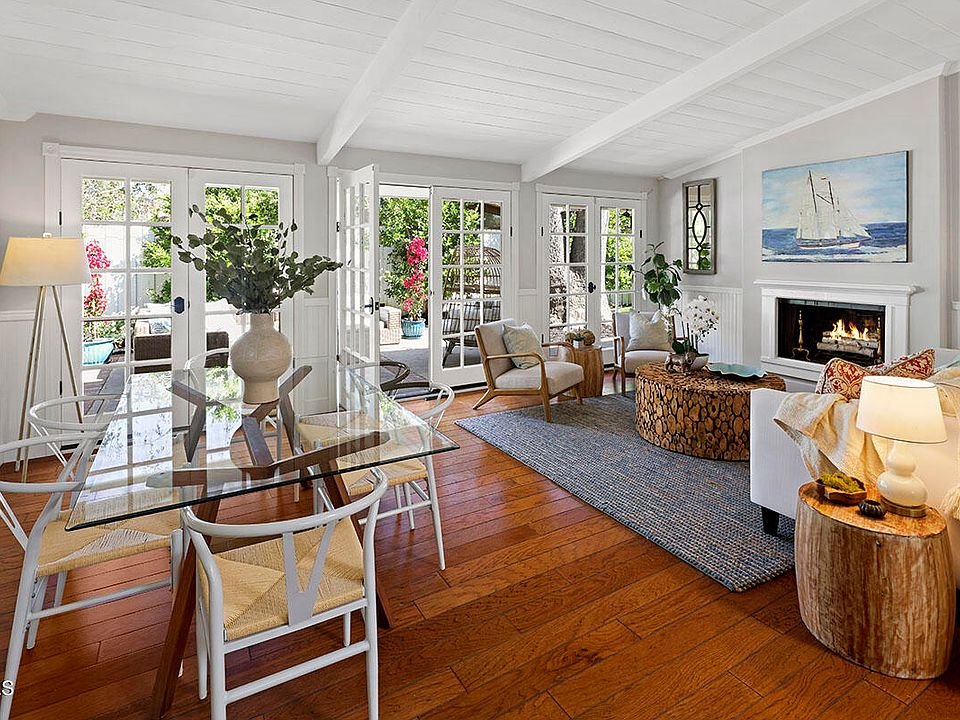 Living room with big windows, glass dining table, chairs, seats, plants, fireplace, and wall art.