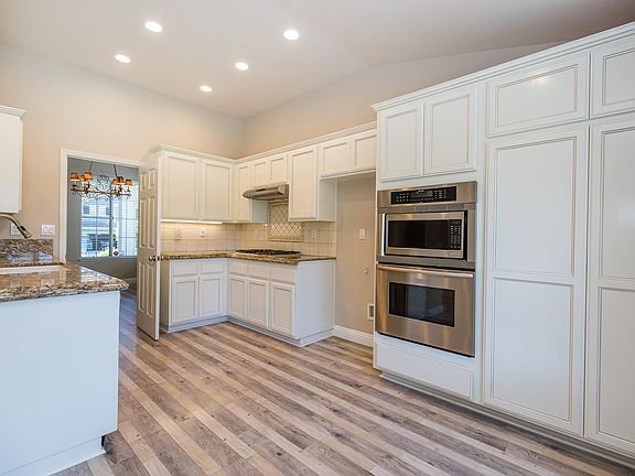 Kitchen with white cabinets, granite countertops, stainless steel appliances, and hardwood floor