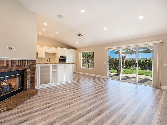 Living room with wall-mounted TV, brick fireplace, sliding glass door, light furniture, and blue rug