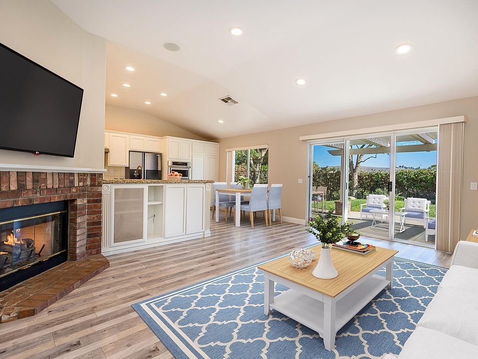 Open living area with fireplace, kitchen with light cabinets and stainless steel appliances, and wood-like floor