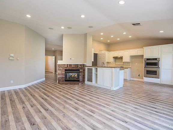 Living room with white sofa, coffee table, blue rug, kitchen with white cabinets and stainless steel appliances, and fireplace