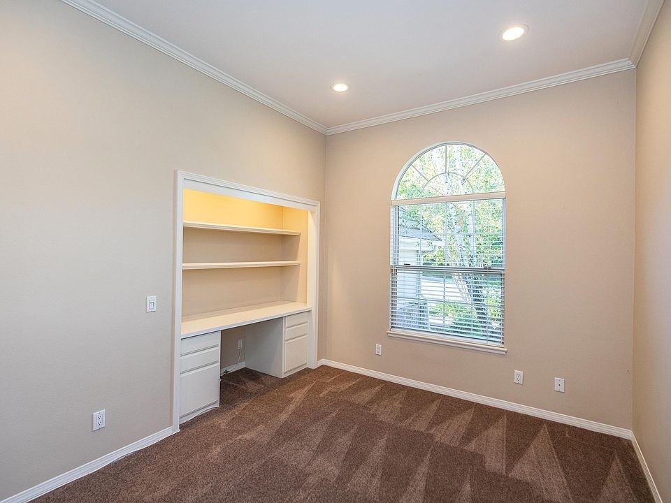 Room with beige walls, carpet floor, built-in shelves, and small desk