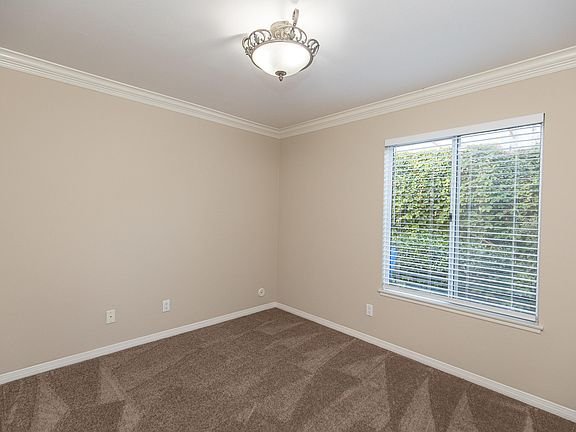 Empty room with beige walls, chandelier light, window with blinds, and carpet floor