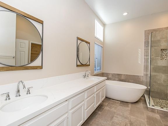 Bathroom with double sink vanity, circular mirrors, freestanding bathtub, and walk-in shower