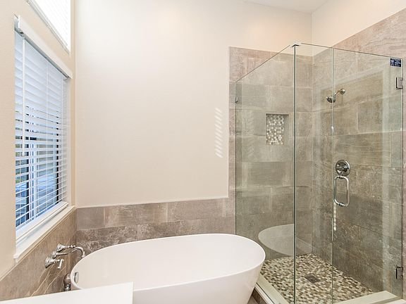 Bathroom with glass shower, freestanding bathtub, and stone tile floor