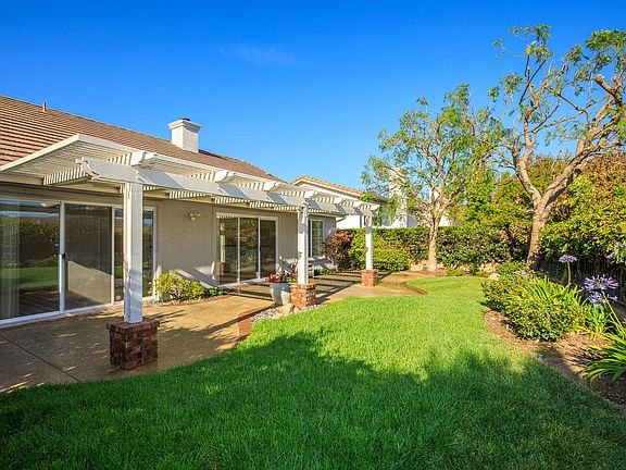 California real estate house backyard with pergola patio, green lawn, trees, and shrubs.