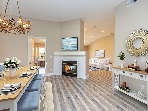 Living room with fireplace, hardwood floor, chandelier, and open layout to another room