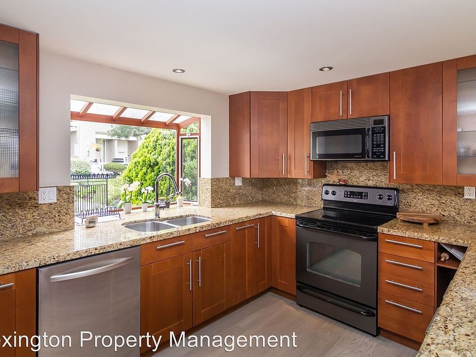 Kitchen with wooden cabinets, granite countertops, stainless steel appliances, and window with view of greenery