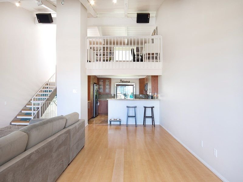 Open living area with staircase, large windows, light walls, hardwood floor, and kitchen with bar stools
