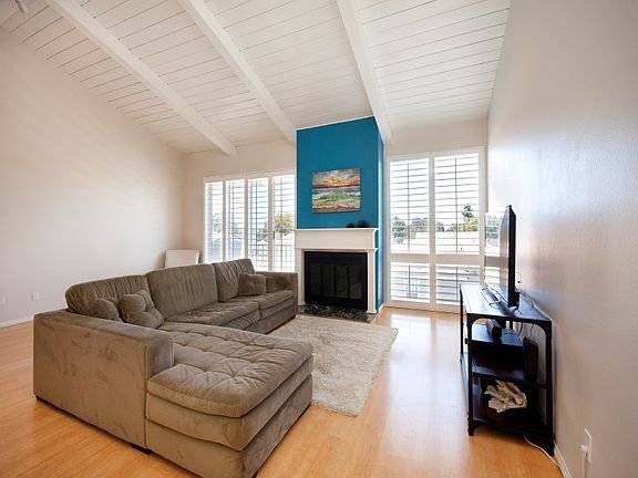 Living room with large sectional couch, fireplace, TV, blue accent wall, and window shutters