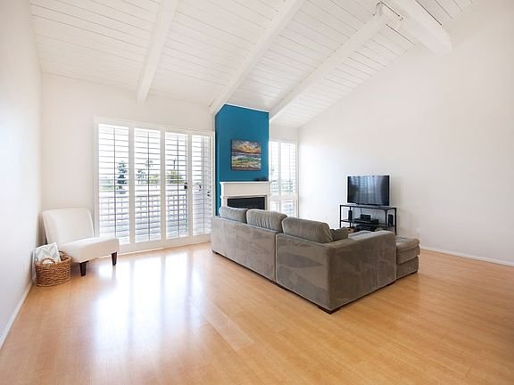 Living room with gray sectional sofa, white chair, black TV stand, blue accent wall, window shutters, and wooden floor