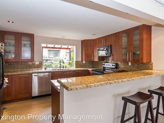 Kitchen with wooden cabinets, granite countertops, stainless steel appliances, and bar seating with stools
