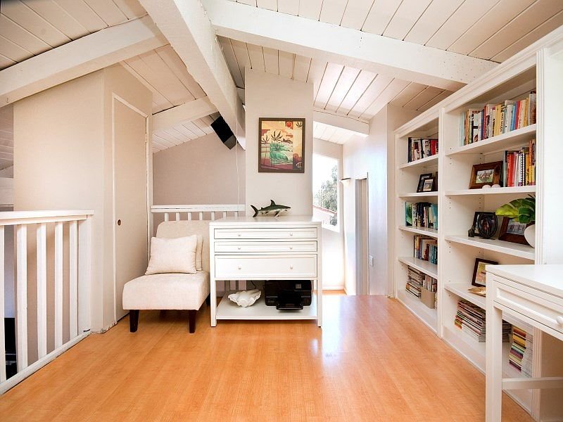 Loft with wooden floor, white chair, chest of drawers, and shelves with books
