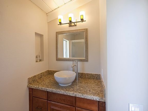 Bathroom with granite countertop, round white vessel sink, large mirror, and wall lighting