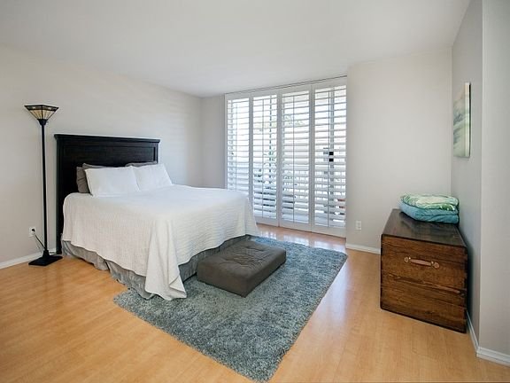 Bedroom with large bed, white bedding, gray rug, window shutters, and wooden dresser