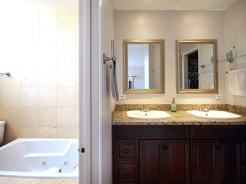 Bathroom with two sinks, granite countertop, bathtub, mirrors, and towel rack