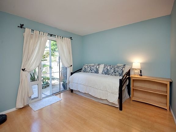 Room with daybed, patterned pillows, wooden shelf, and large windows with sheer curtains