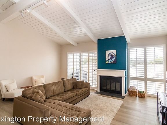 Living room with large brown sectional sofa, fireplace with blue accent wall, white-beamed ceiling, and window shutters