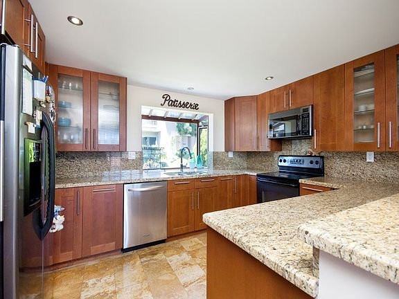 Kitchen with wooden cabinets, granite countertops, stainless steel appliances, and window above sink