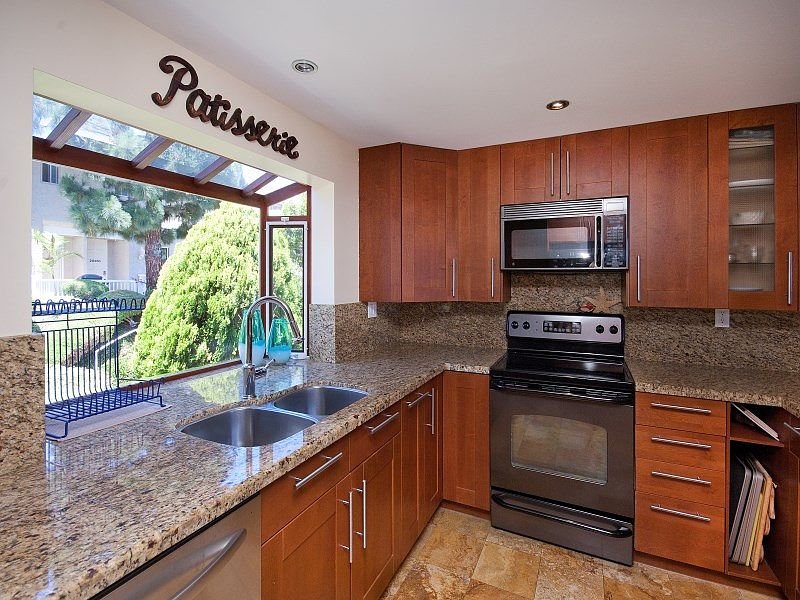 Kitchen with wooden cabinets, granite countertop, stainless steel appliances, and window with view of greenery