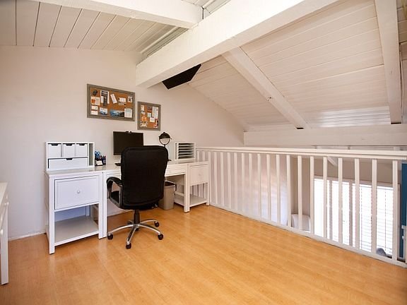 Home office with wooden floor, modern desk, black chair, computer, and wall decor