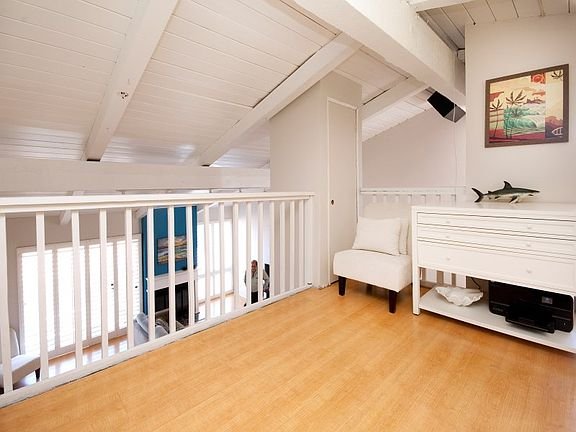 Room with wooden floor, white walls, vaulted ceiling, armchair, drawer, and wall painting