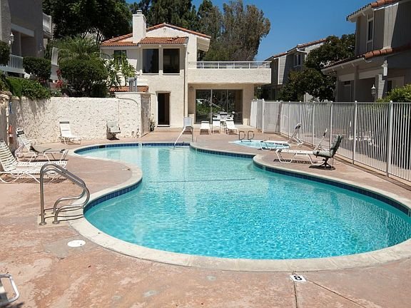 Swimming pool with lounge chairs, white fence, and houses in the background