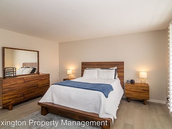Bedroom with wooden bed, white bedding, nightstands with lamps, and dresser with mirror