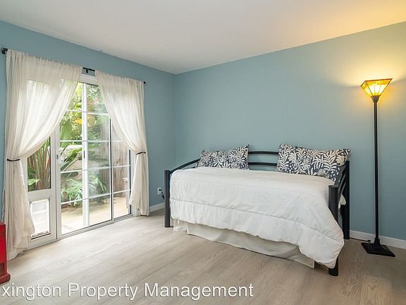 Room with daybed, white bedding, decorative pillows, floor lamp, and glass doors to patio