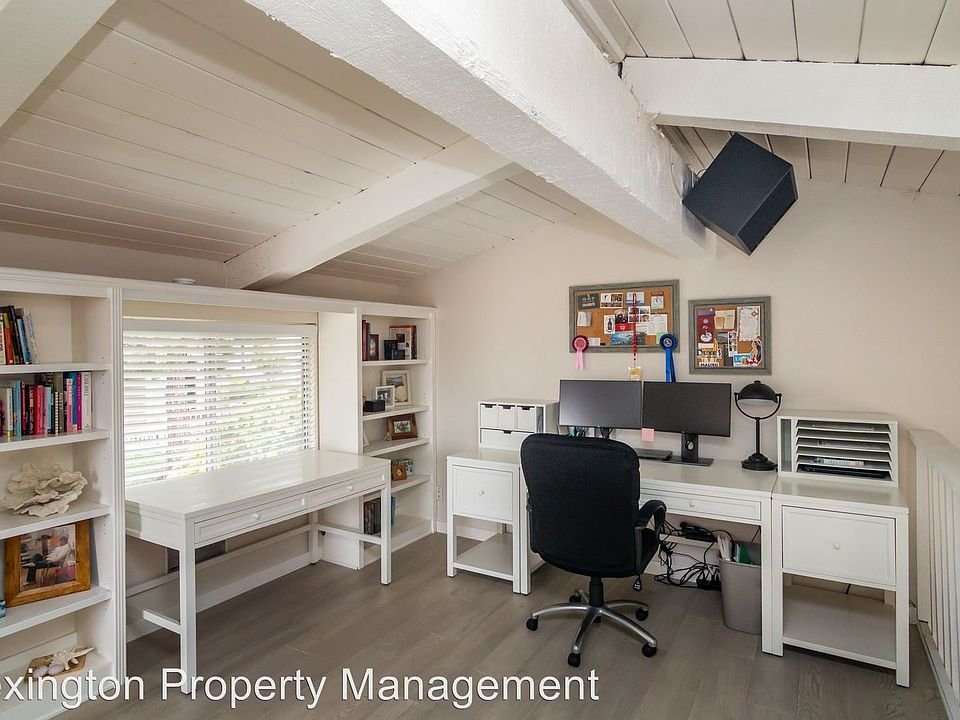 Office with white desk and chair, bookshelves with books, bulletin board, exposed beams, and window light