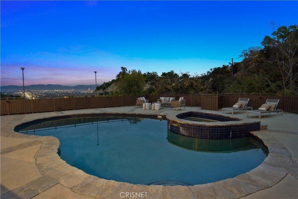 Pool area with hot tub, lounge chairs, and city view.