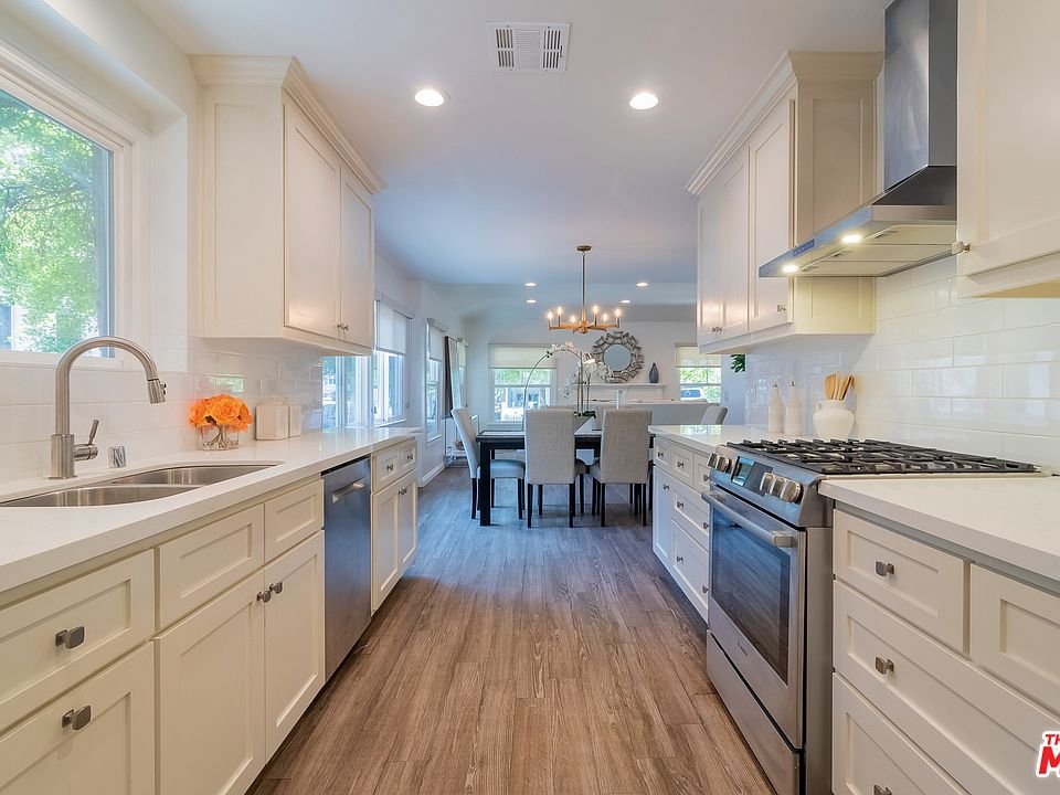 Kitchen with white cabinets, island stove, table, chairs, and wood floor.