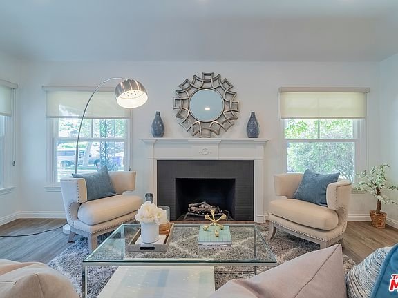 Living room with armchairs, glass coffee table, fireplace, mirror, and windows.