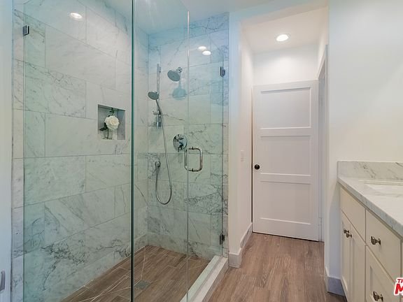 Bathroom with glass shower, marble walls, rainfall shower, and wood floor.
