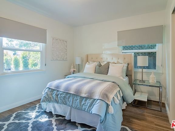 Bedroom with bed, pillows, nightstand, wooden floor, and windows.