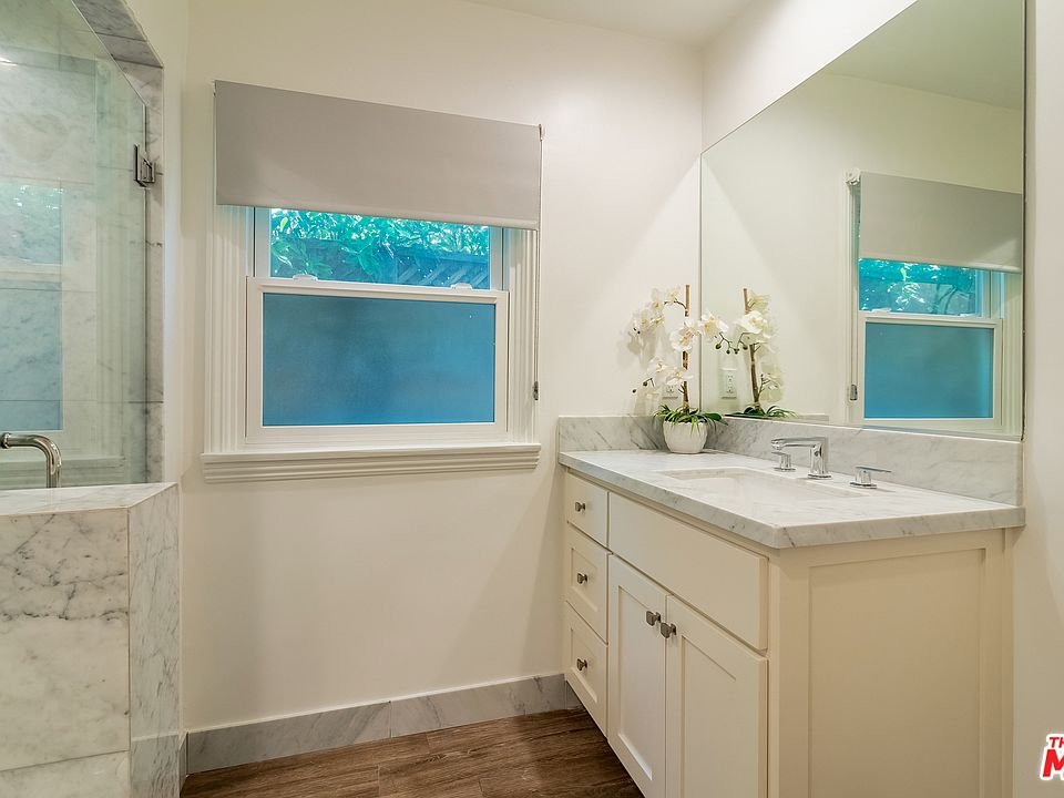 Bathroom with marble counter, mirror, orchids, window, and wood floor.